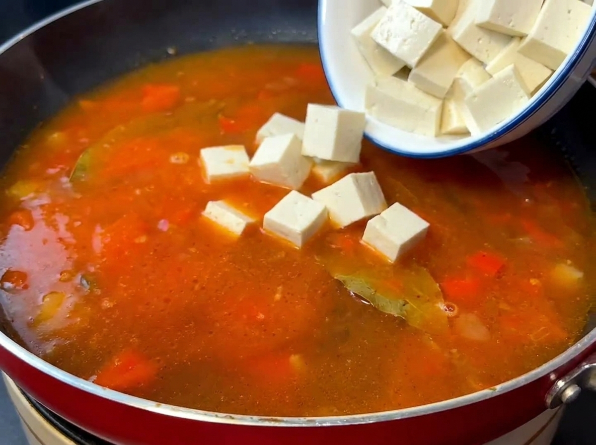 Cubetti di tofu di seta e manzo saltato aggiunti alla base di pomodoro in cottura.