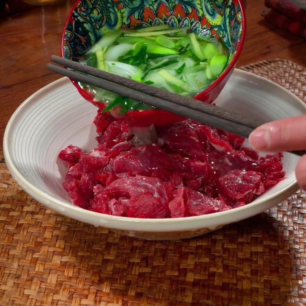 Strisce di manzo crudo condite e massaggiate a mano in una ciotola di ceramica.