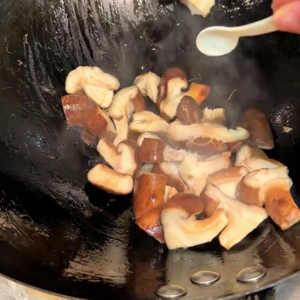 Condimento dei funghi shiitake che saltano nel wok con sale e salsa di soia usando un cucchiaino.
