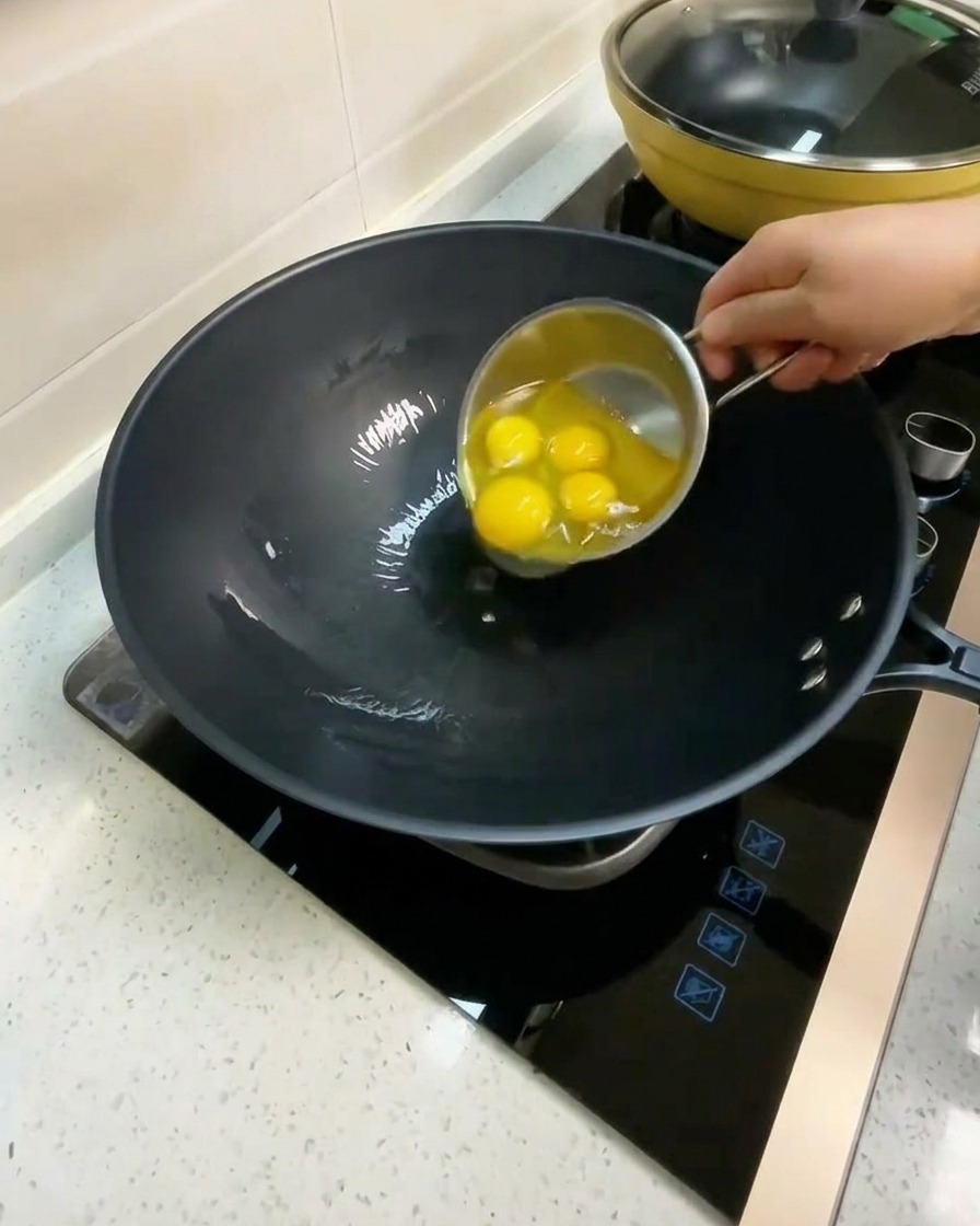 Quattro uova crude rotte in un wok con olio caldo.