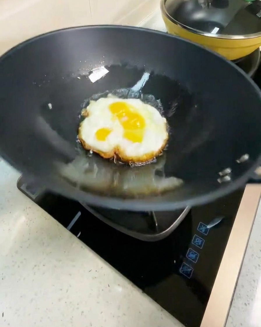 Uovo fritto girato in un wok caldo, che mostra il lato inferiore marrone dorato.