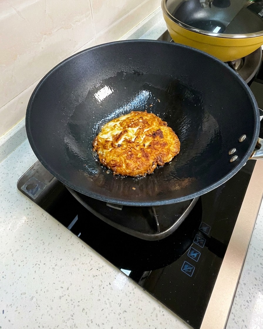 Uova fritte in un wok spezzettate in pezzi grandi con una spatola di metallo.