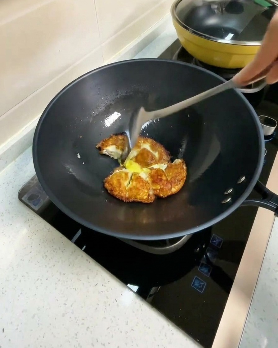Acqua calda versata in un wok contenente pezzi di uovo fritto.