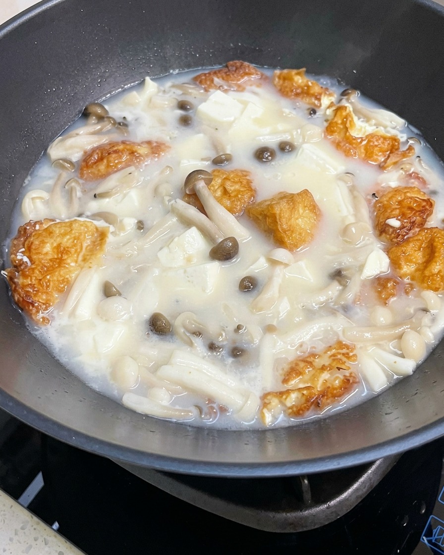 Un primo piano della zuppa di funghi e tofu che sobbolle in una padella mentre viene condita con sale e pepe.