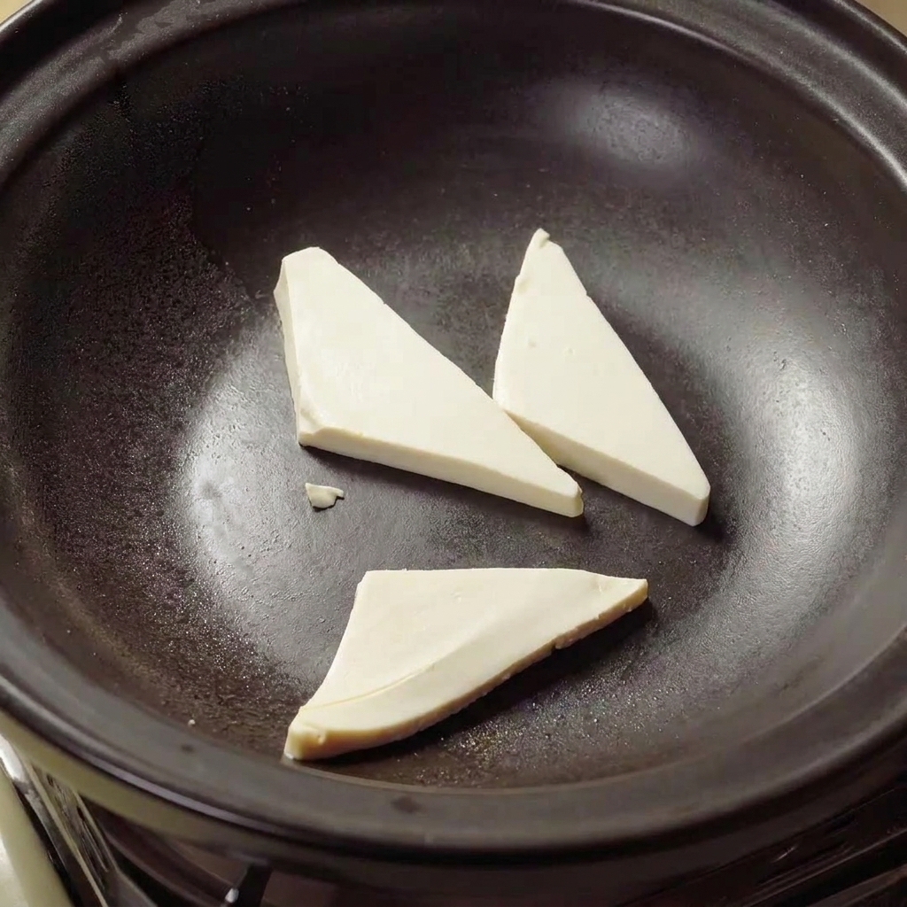 Triangoli di tofu che friggono in olio caldo allinterno di una pignatta di terracotta fino a diventare dorati.