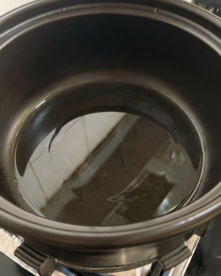 Una pentola nera sul fornello con una piccola quantità di olio che inizia a scaldarsi sul fondo.