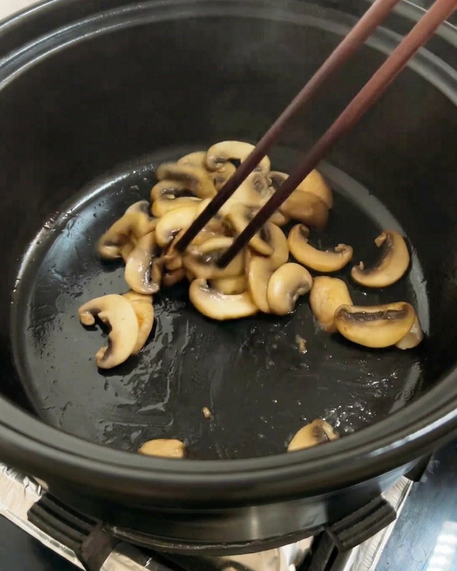 Pomodori rossi tritati aggiunti alla pentola insieme ai funghi rosolati, pronti per essere saltati.