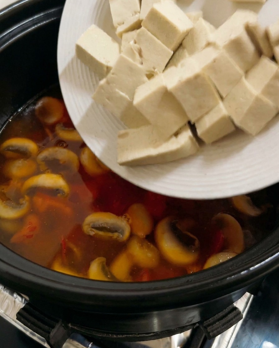 Cubetti di tofu bianco compatto aggiunti a una zuppa di pomodoro e funghi che bolle.