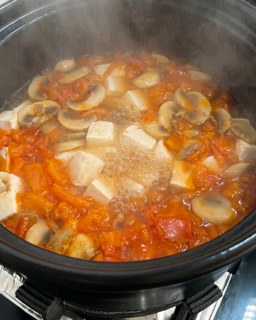 Una pentola di zuppa di pomodoro e funghi con tofu, in cui viene versato a filo delluovo sbattuto.