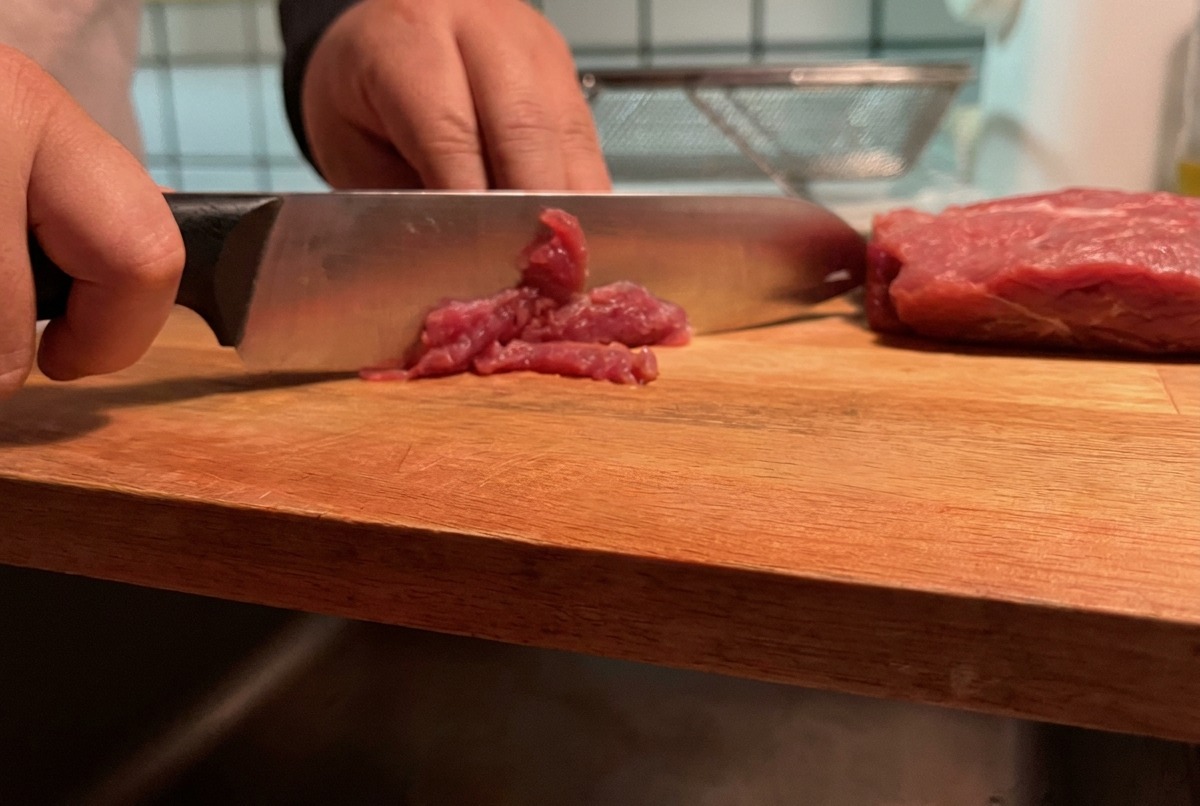 Maiale magro tagliato a strisce sottili su un tagliere di legno.
