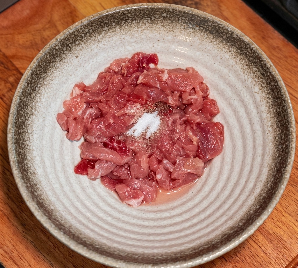 Strisce di carne cruda in una ciotola con spezie e amido sopra.