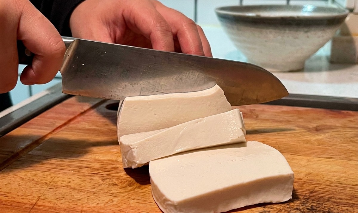 Un panetto di tofu bianco tagliato a cubetti su un tagliere.