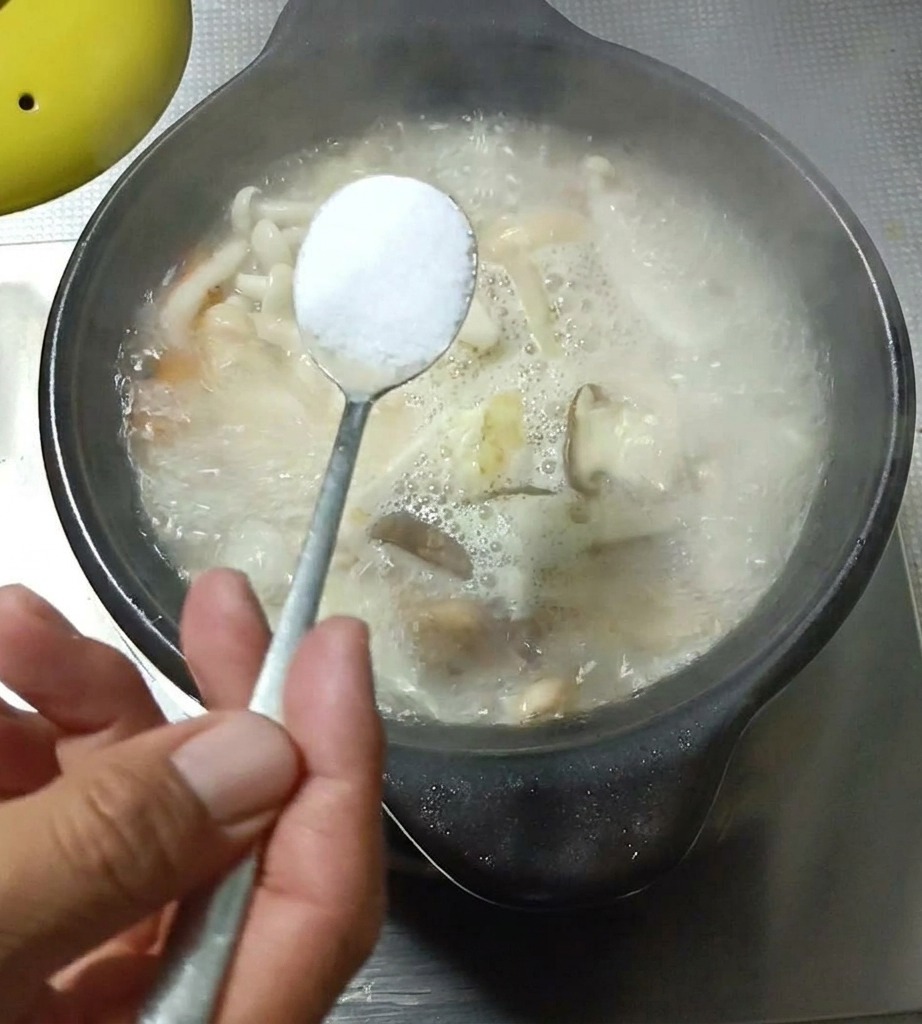 Primo piano di un cucchiaio di condimento aggiunto alla zuppa in ebollizione.