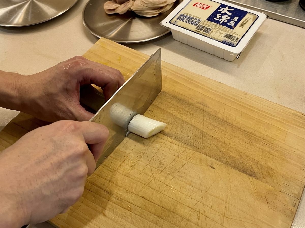 Cipollotti freschi affettati su un tagliere di legno con un coltello.