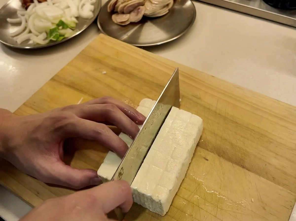 Blocco di tofu tagliato a fette uniformi su un tagliere di legno.