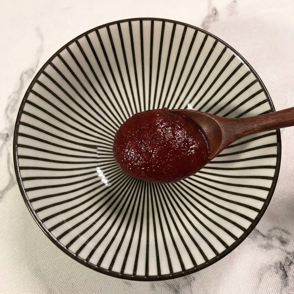 Un cucchiaio di legno che aggiunge una dose di pasta di peperoncino coreano in una ciotola a righe.