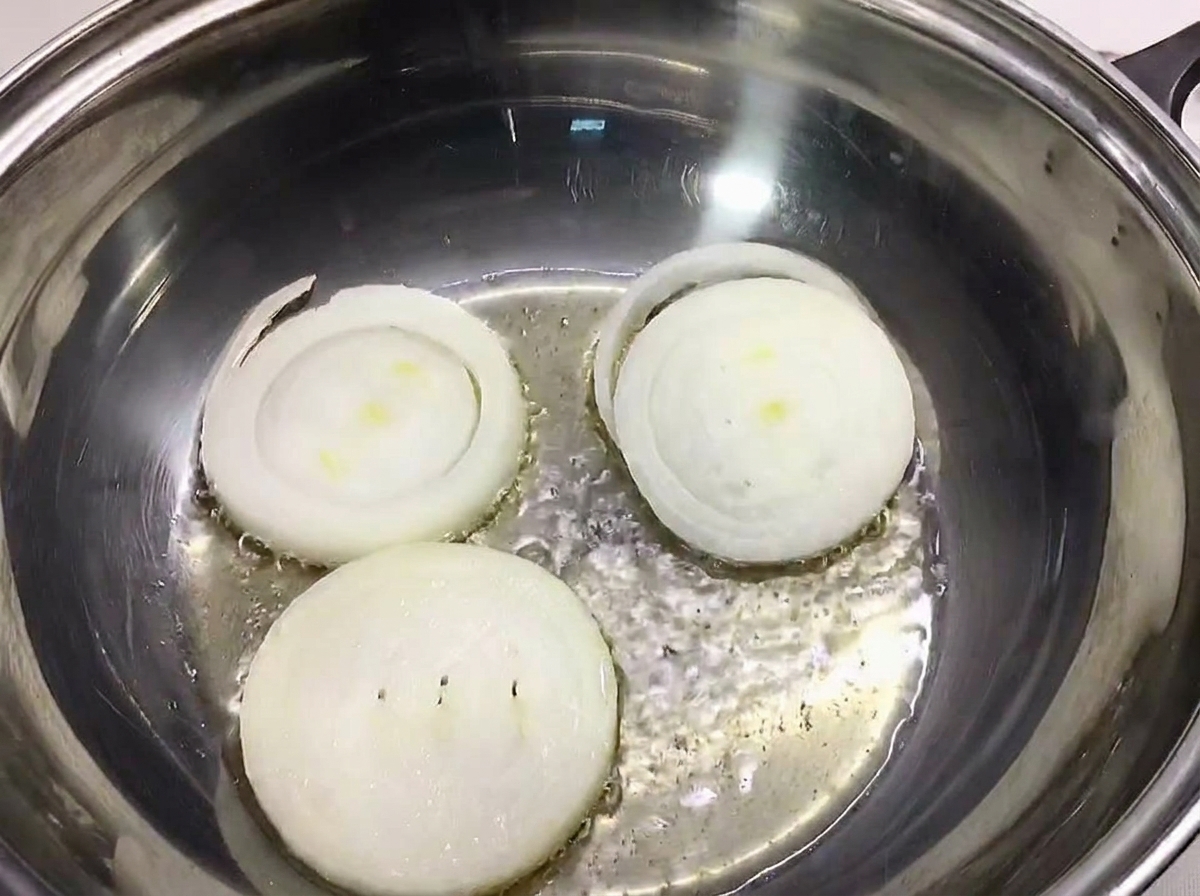 Tre fette spesse di cipolla bianca sul fondo di una pentola in acciaio inossidabile.