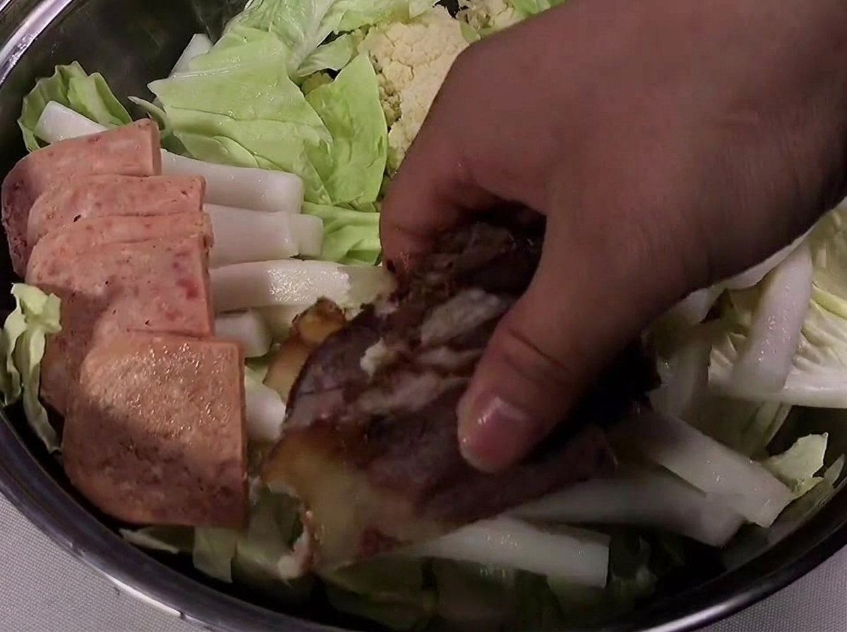 Fette di Spam, manzo cotto e salsiccia disposte ordinatamente lungo il bordo della pentola.