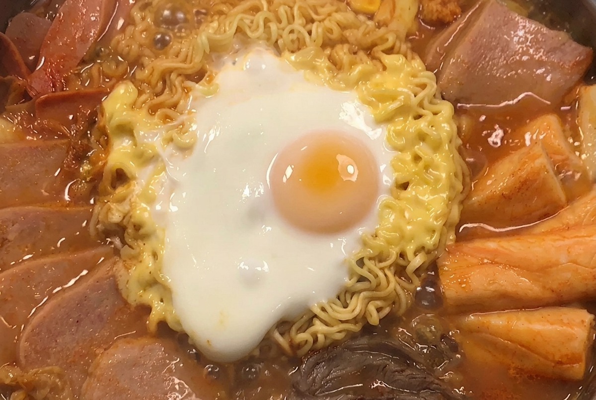 Una pentola fumante di stufato guarnita con chicchi di mais e cipollotti affettati.