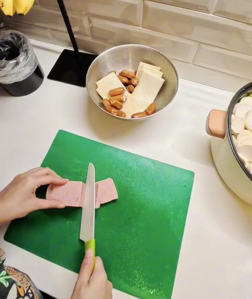 Fette di carne in scatola e tortini di pesce disposti su un tagliere, a dimostrazione della preparazione degli ingredienti principali dello stufato.