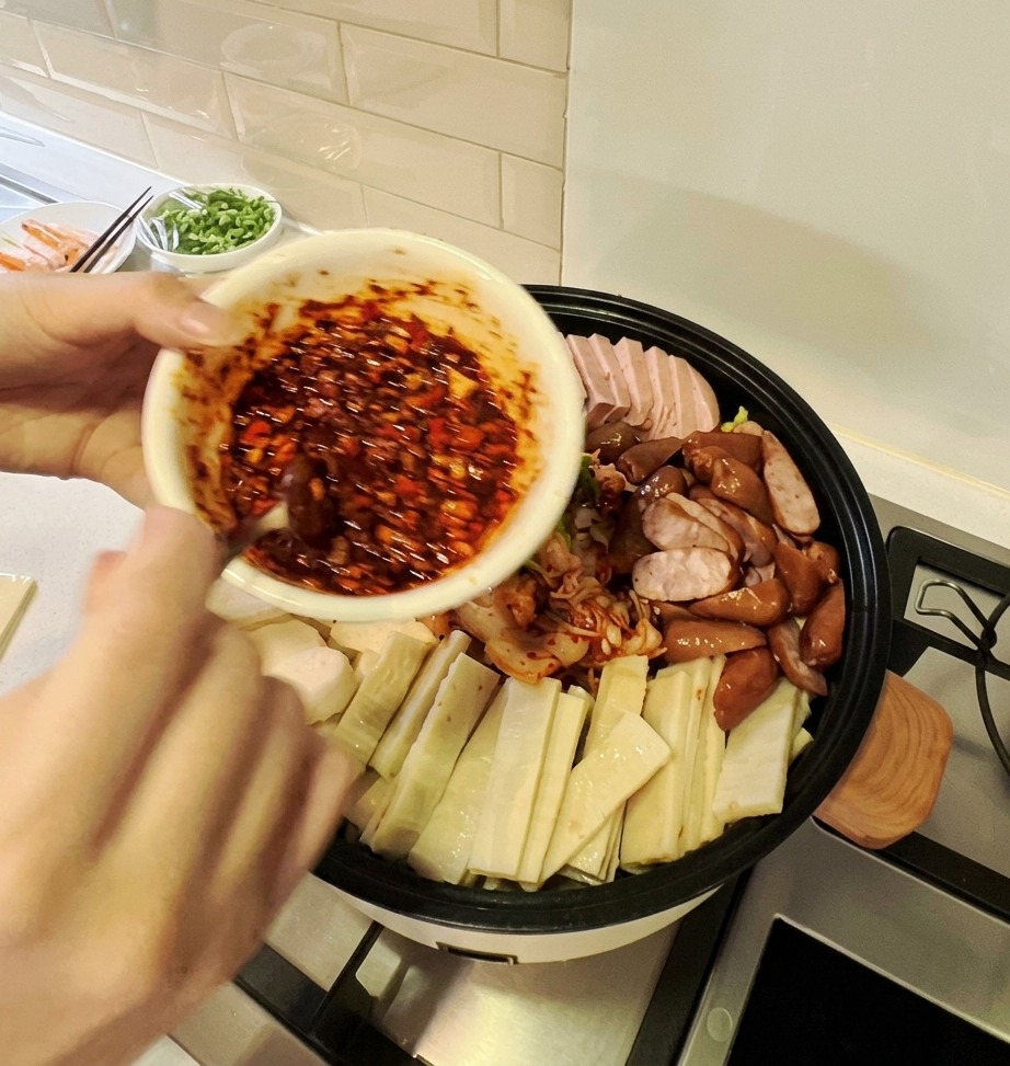 Una ciotola di vibrante salsa rossa piccante versata sulla disposizione colorata di ingredienti in una grande pentola per stufato coreano.