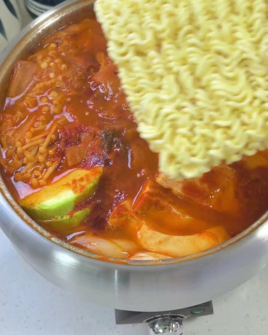 Uno stufato coreano quasi pronto guarnito con noodle ramen, fette di formaggio giallo e un uovo.