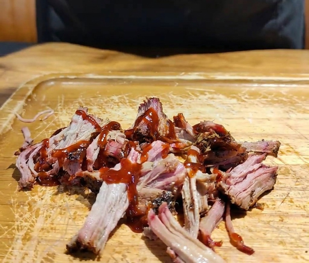 Una mano aggiunge un mix di cavolo viola e bianco sminuzzato sopra il maiale condito con salsa BBQ.