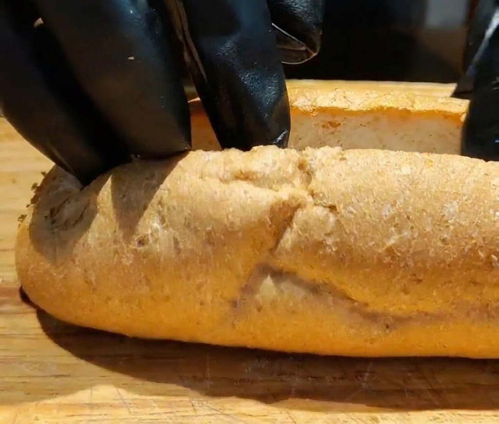 Primo piano di mani che aprono una baguette integrale tostata per creare spazio per il ripieno.