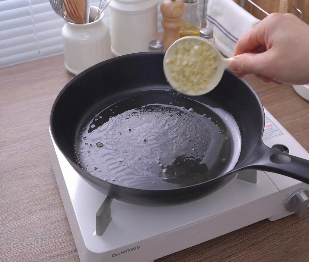 Una ciotolina versa aglio tritato in una padella con burro fuso.
