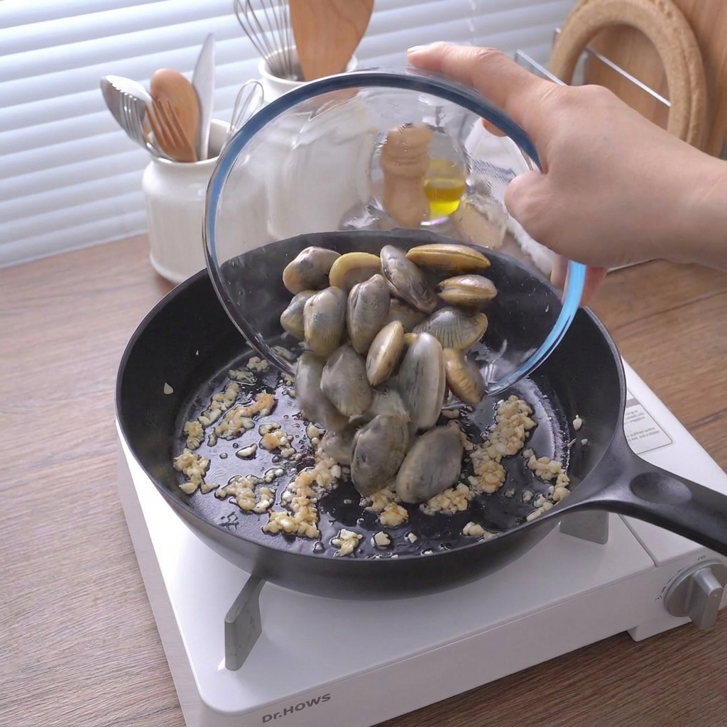 Una ciotola di vetro versa vongole pulite in una padella con soffritto di aglio.
