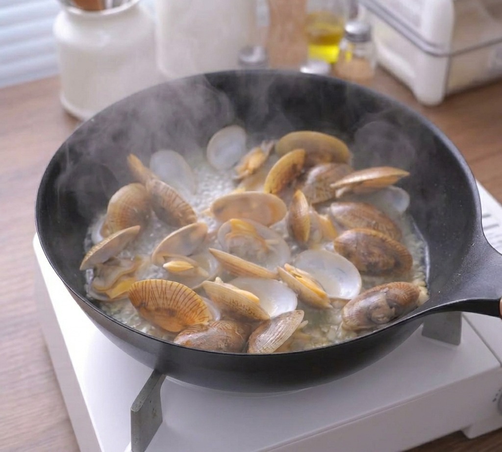Vapore che sale da una padella nera con molte vongole completamente aperte e cotte.