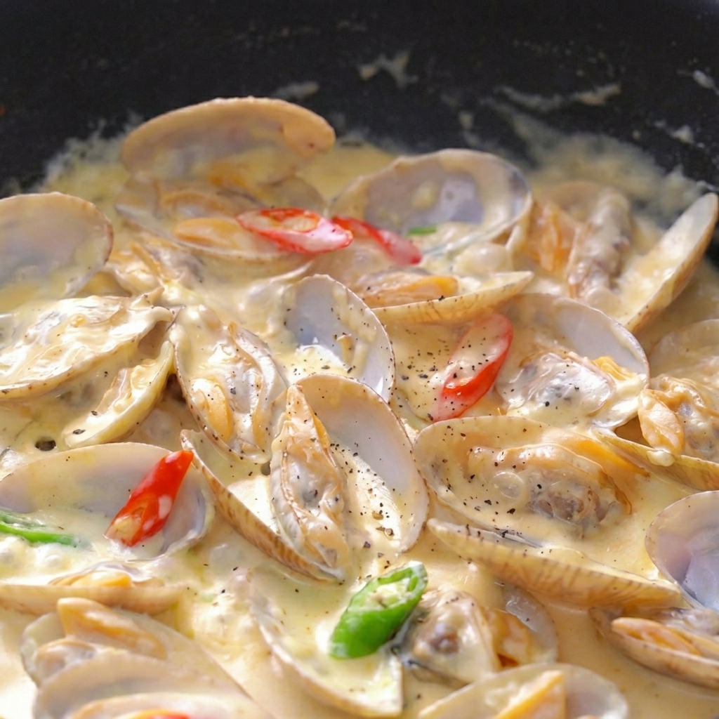 Primo piano di vongole in salsa densa con pepe nero, prezzemolo e peperoncino.