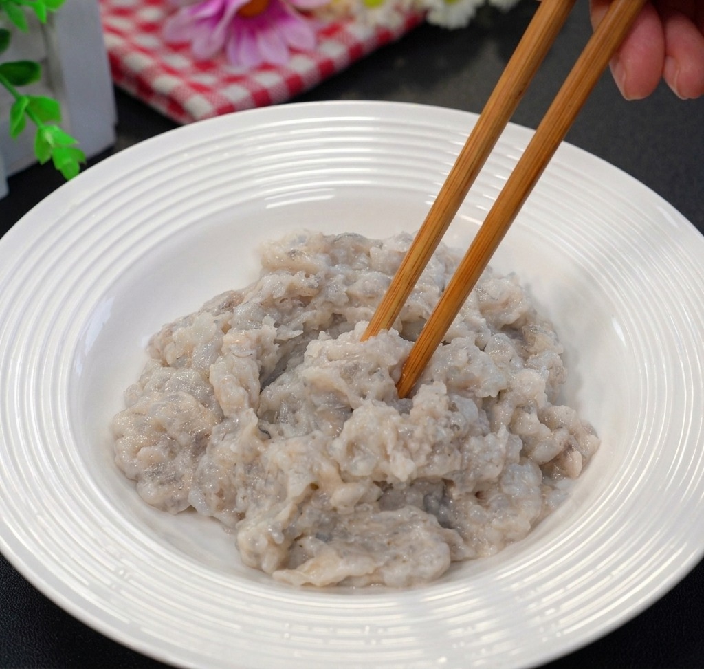 Polpa di gamberi tritata mescolata con bacchette di legno in una ciotola di ceramica bianca.