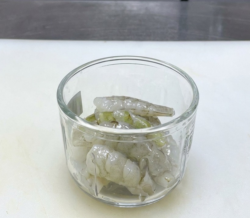 Gamberi crudi traslucidi in un contenitore di vetro su un tagliere bianco pulito.