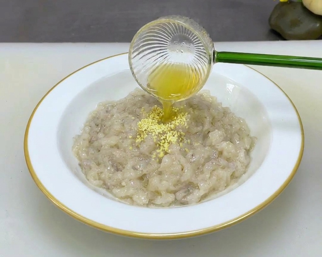 Una persona versa polvere gialla da un cucchiaino in una ciotola bianca con pasta densa di gamberi.