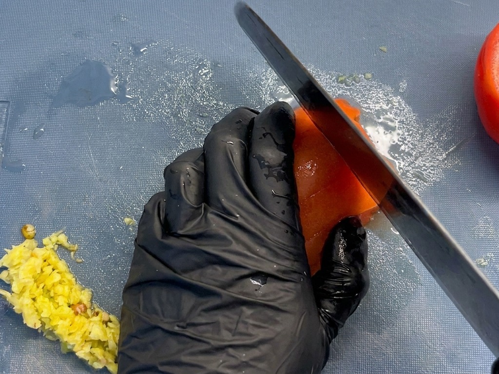 Primo piano di uno chef che taglia un pomodoro pelato in cubetti uniformi su un tagliere blu.