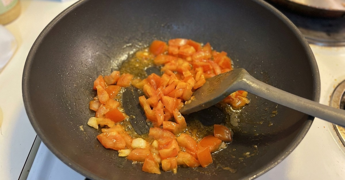 Cubetti di pomodoro saltati con aglio in un wok scuro, con i succhi che iniziano a bollire sul fondo.