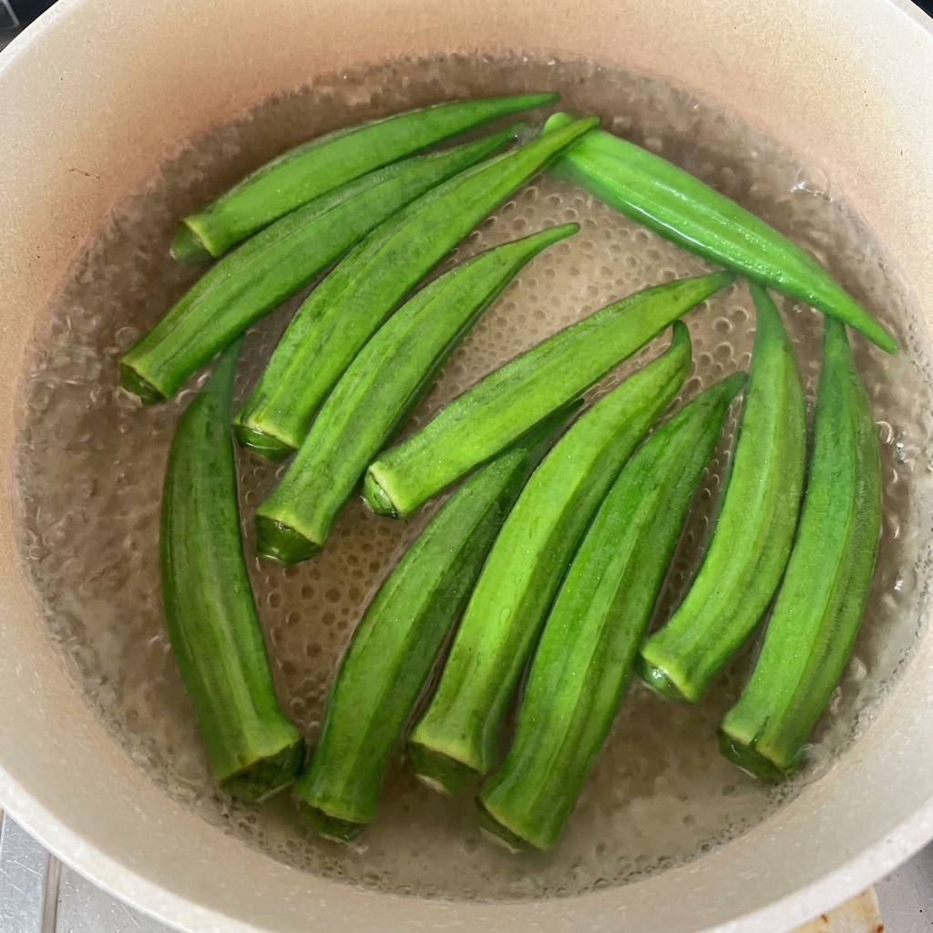 Baccelli di okra verde fresca che galleggiano in una pentola dacqua bollente.