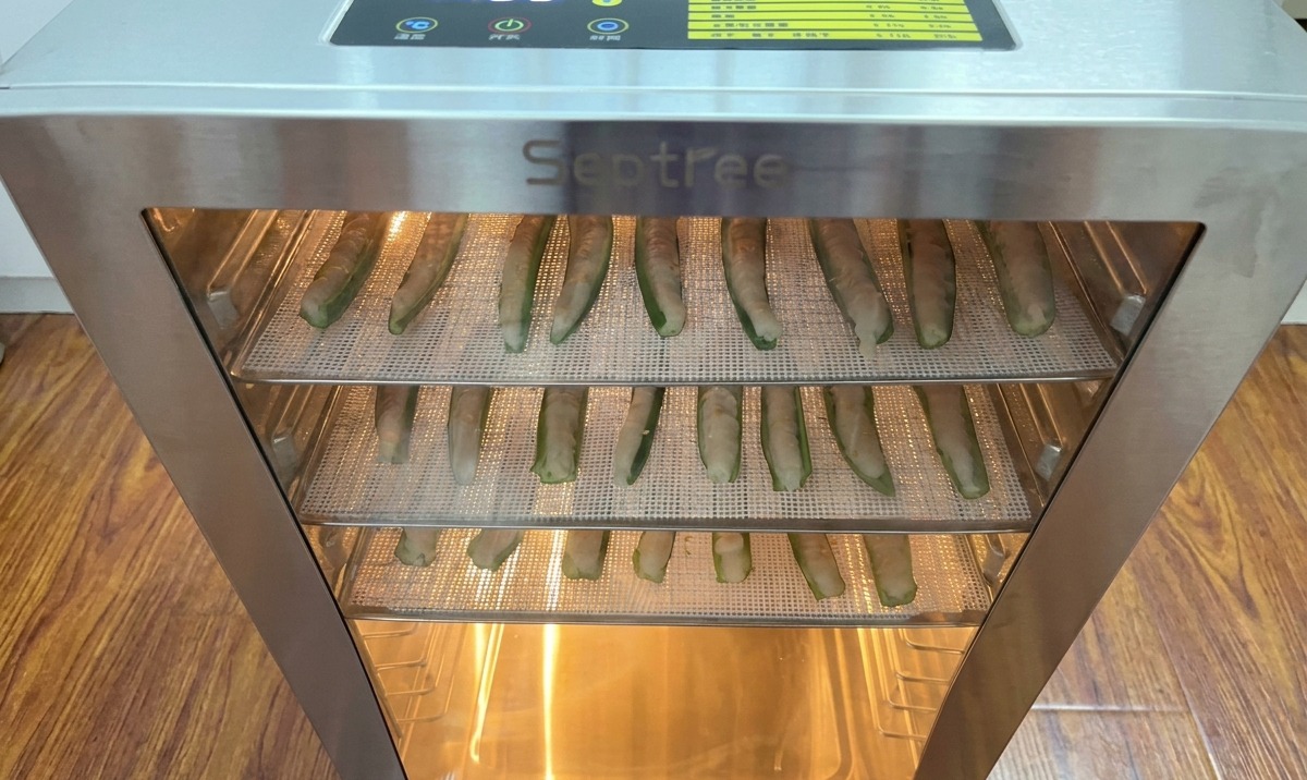 Ripiani di okra farcita con pollo inseriti in un essiccatore in acciaio inox con timer digitale.