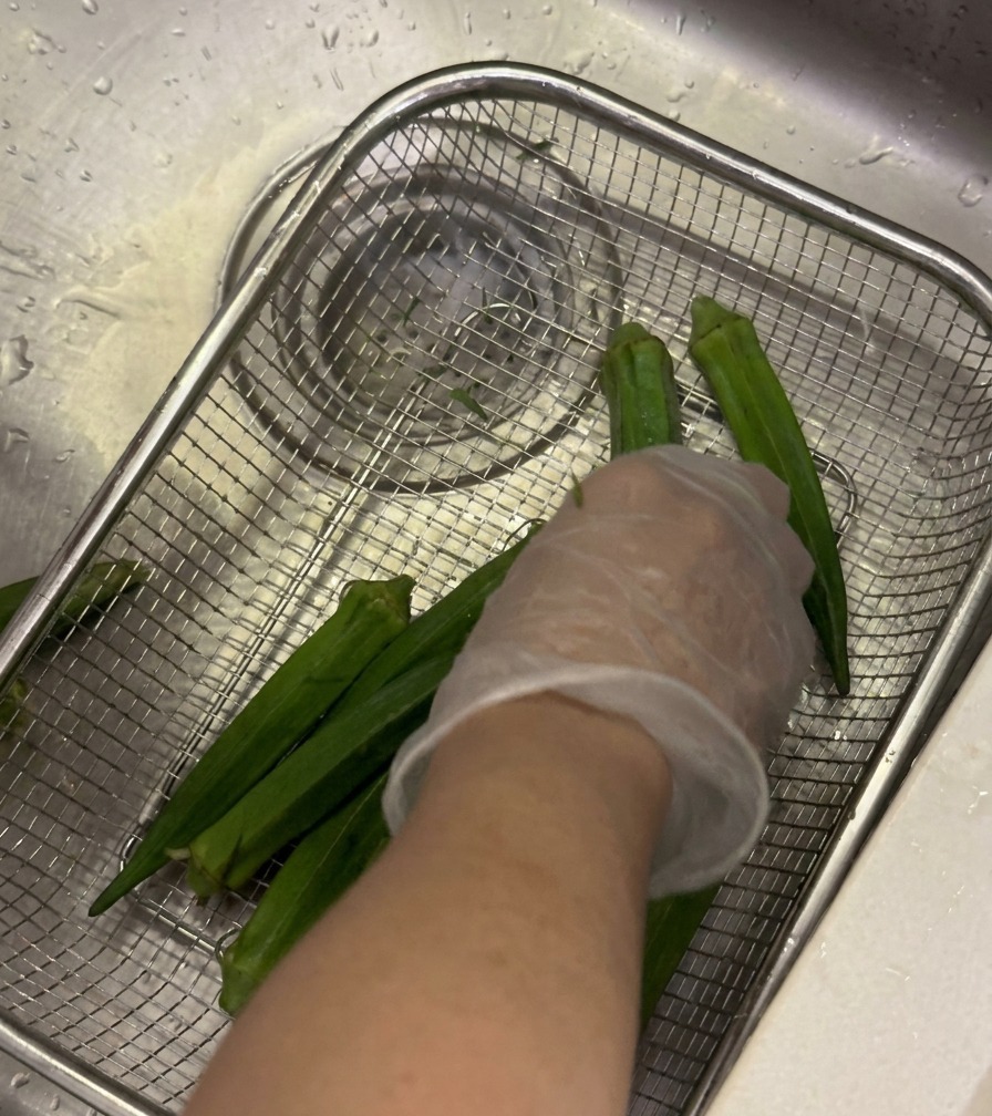 Baccelli di okra freschi lavati sotto acqua corrente in un colino, strofinati delicatamente con una mano.