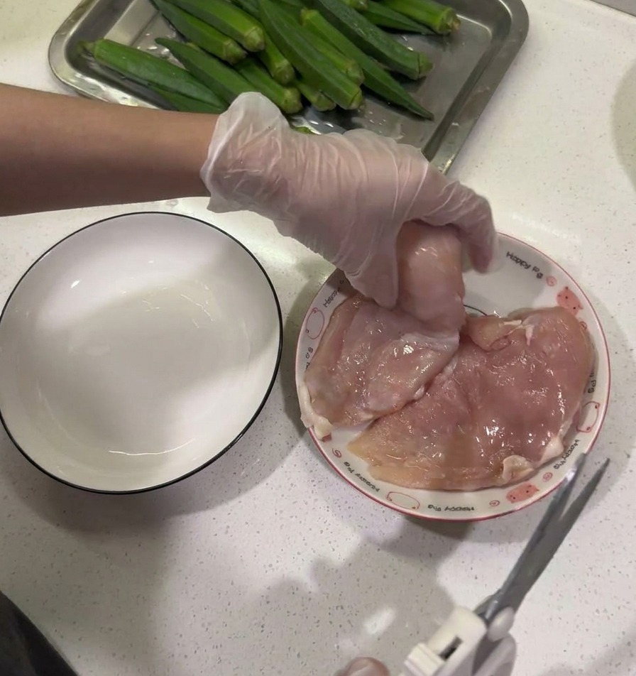 Forbici da cucina utilizzate per rimuovere il grasso da un petto di pollo crudo su un piatto bianco.