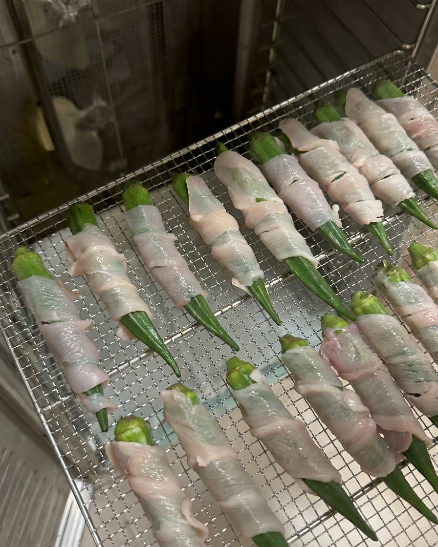 Baccelli di okra avvolti nel pollo disposti ordinatamente su una griglia metallica allinterno di un essiccatore.