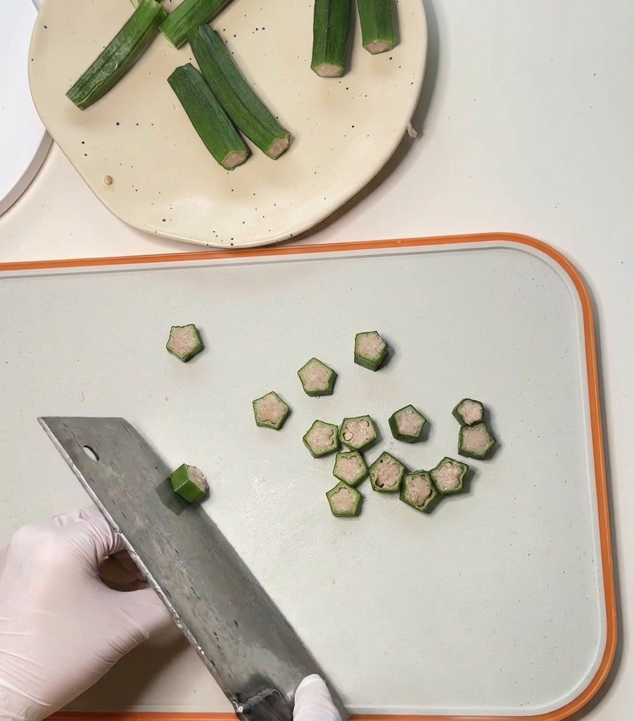Una grande mannaia di metallo che taglia i baccelli di okra farciti di pollo in piccole rondelle a forma di stella.