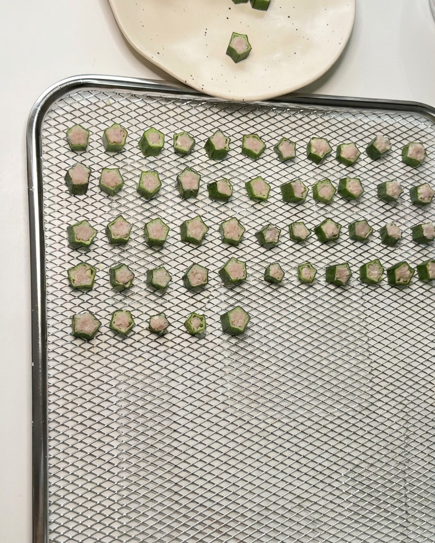 Decine di snack di okra e pollo a forma di stella disposti in file ordinate su un vassoio a rete per essiccatore.
