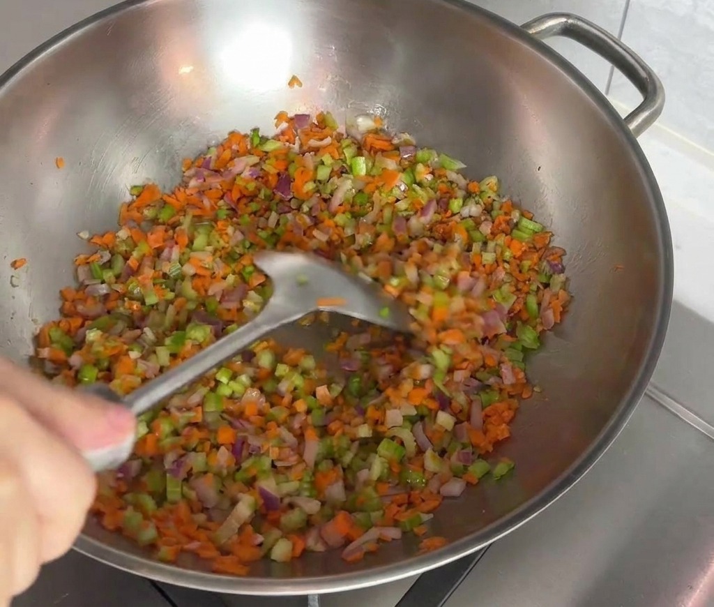 Un mix colorato di carote, sedano e cipolle rosse viene saltato con una spatola in un wok dacciaio inox.