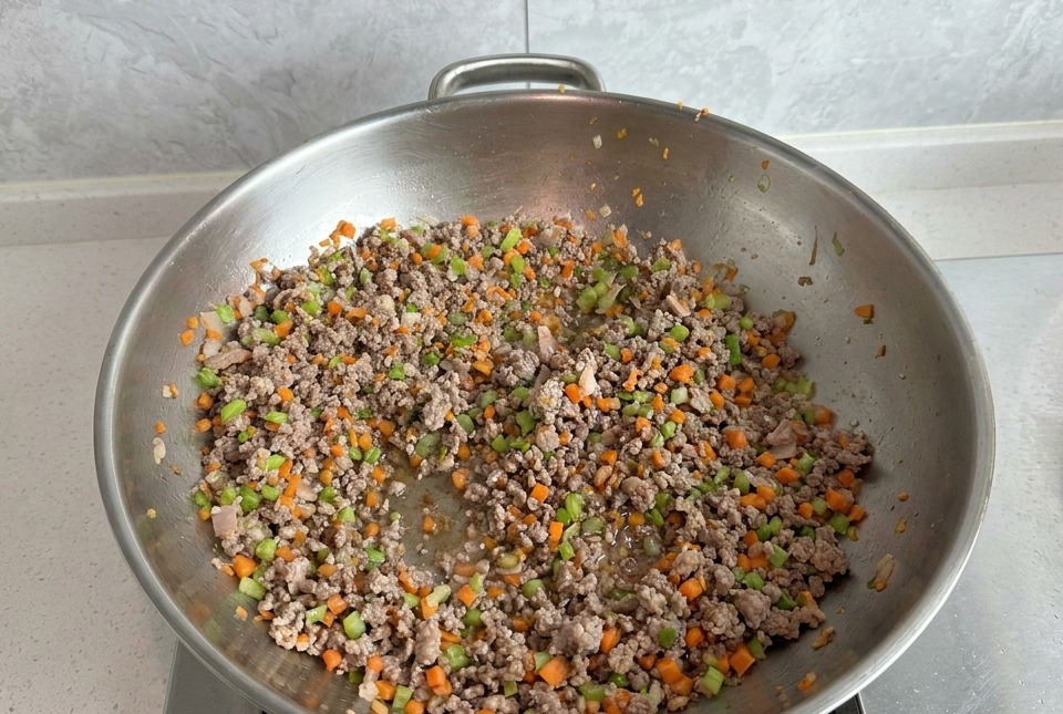 Carne macinata saltata con carote e sedano in un grande wok dargento, con la carne che appare perfettamente rosolata.