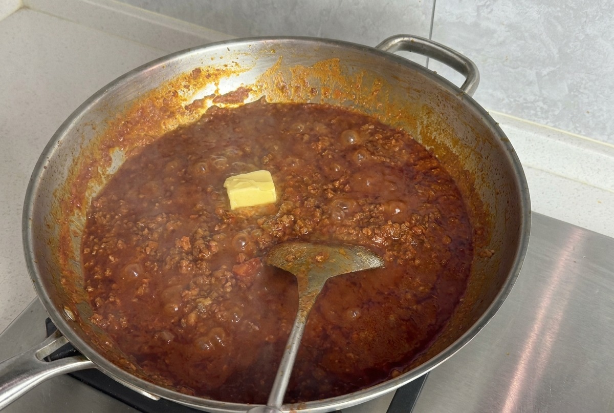 Un cubetto giallo di burro sulla superficie di un ragù di pomodoro e carne in una grande padella dargento.