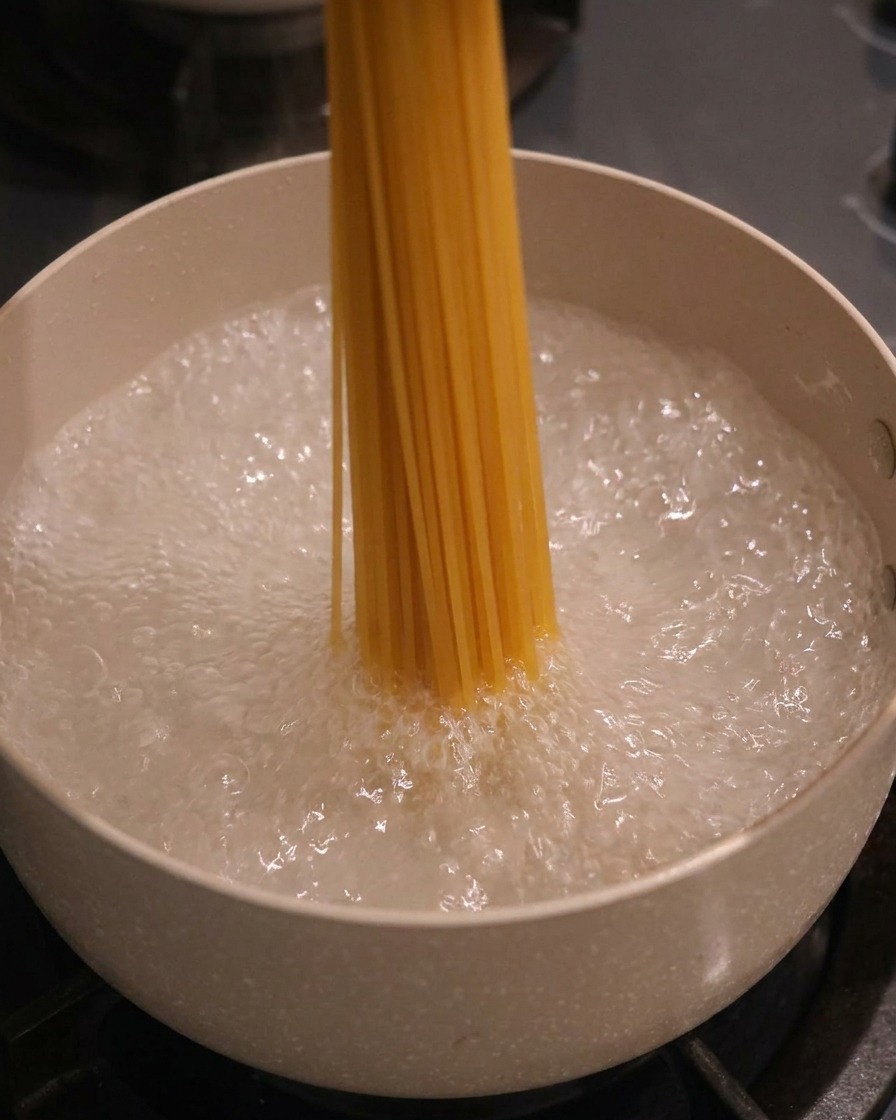 Un mazzo di spaghetti secchi immersi verticalmente in una pentola dacqua bollente e spumeggiante.