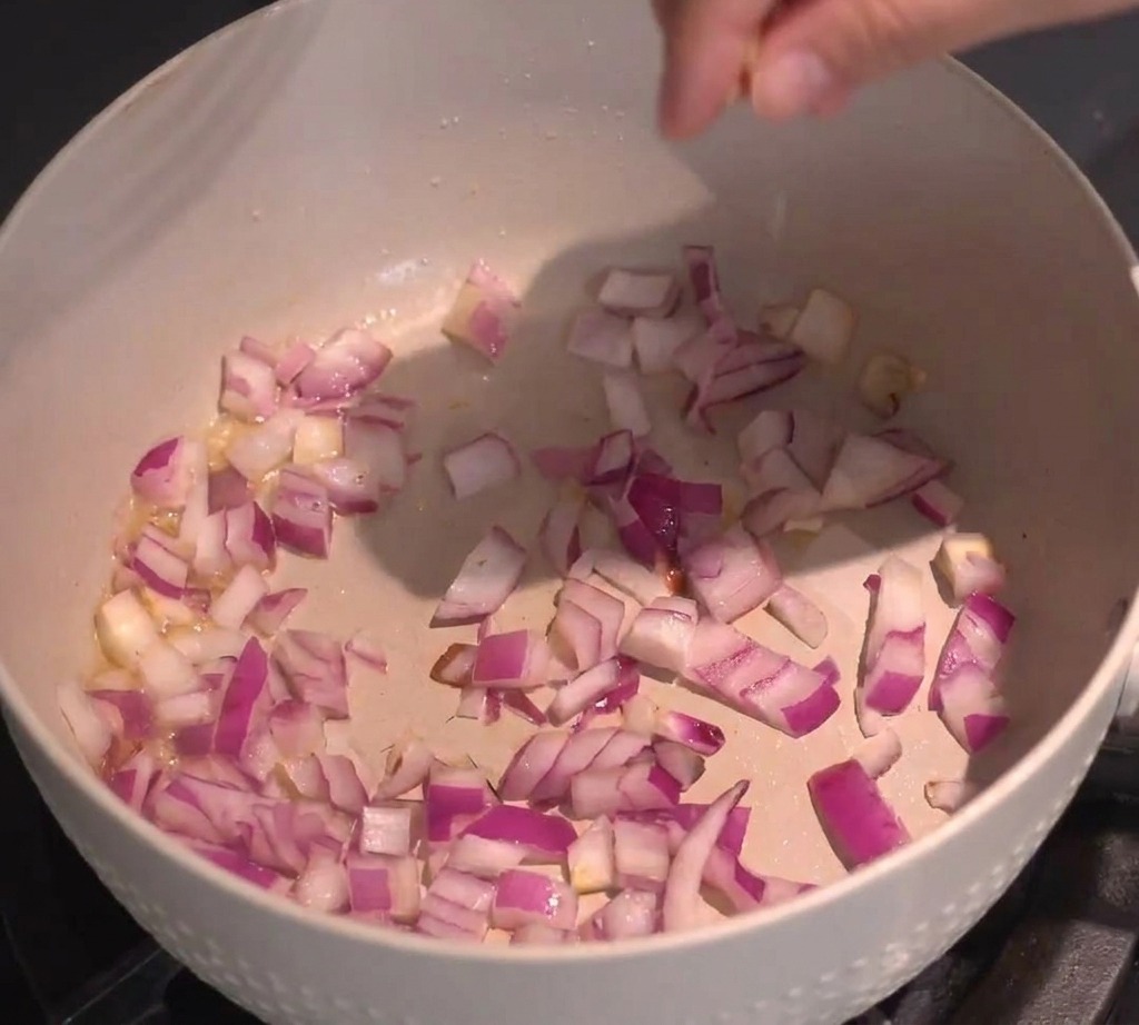 Dadini di cipolla rossa fatti saltare in una padella di colore chiaro sul fornello.