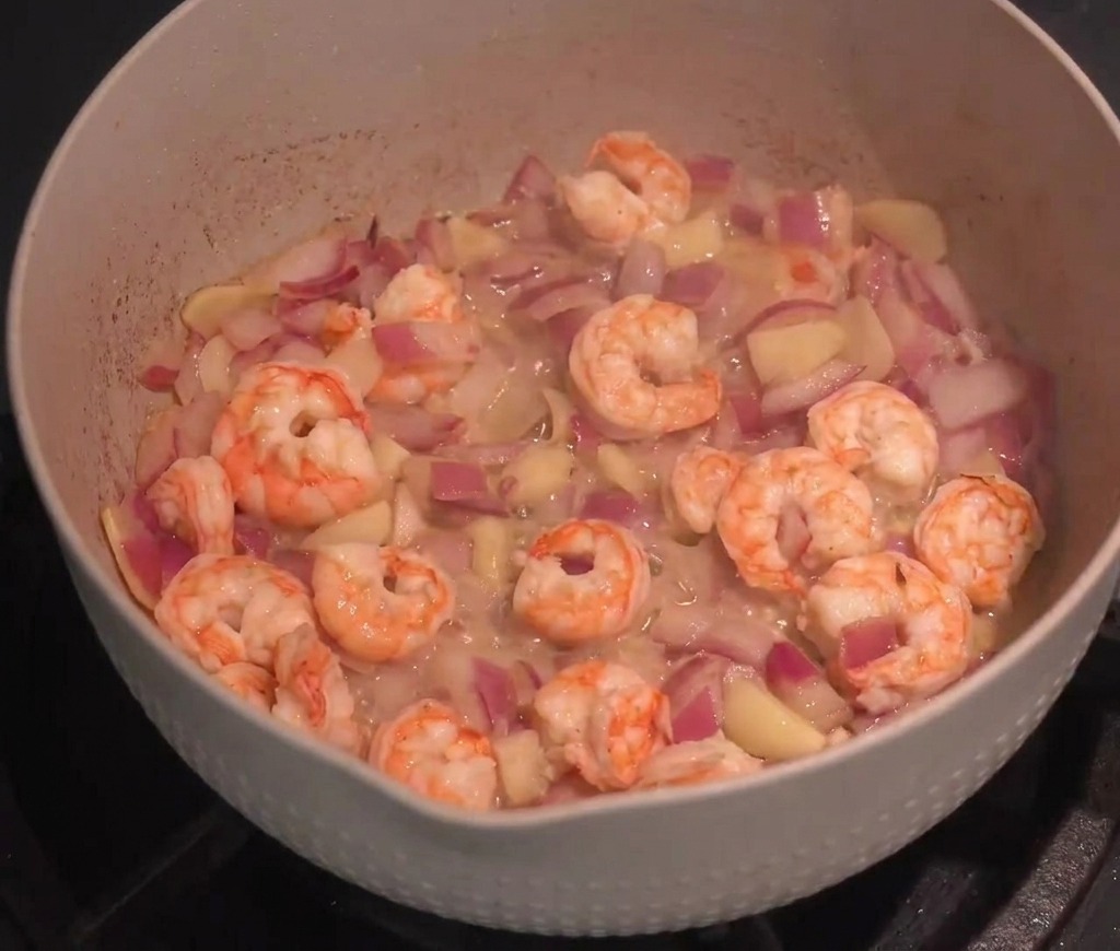 Gamberi freschi saltati con cipolla e aglio in una padella capiente con salsa rossa.